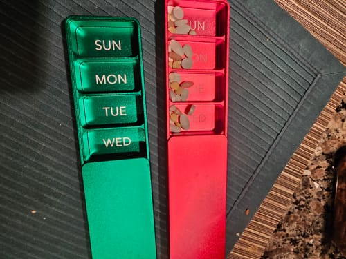 A reviewer's green and red Weekly Vitamin Cases. The red case is open with pills, while the green one is closed.