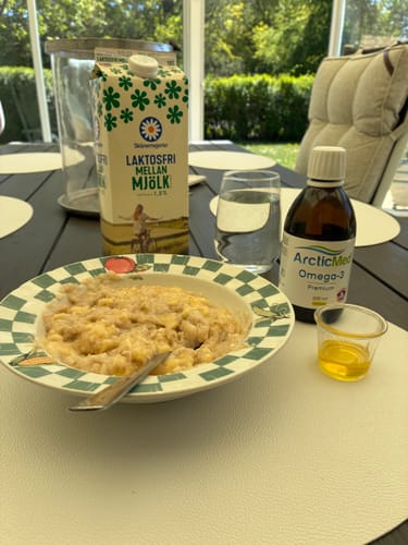 Kundens Omega-3 Premium-flaska och en uppmätt dos olja på ett frukostbord.