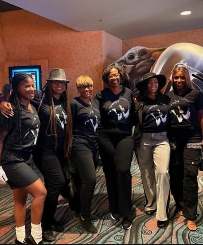 A group of reviewers smiling and posing together at an event while wearing their matching black MJ shirts.