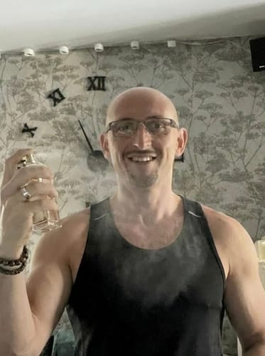 Reviewer in a black tank top smiles while spraying the Inspired by Black Orchid - 19 perfume.