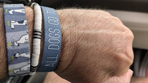 Close-up of a customer wearing the blue All Dogs Go To Heaven Bracelet stacked with other bracelets on their wrist.