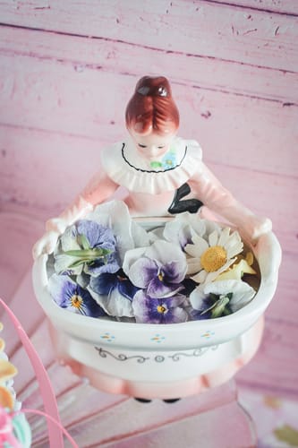 Customer's Light Purple Violas displayed in a decorative ceramic bowl held by a figurine.