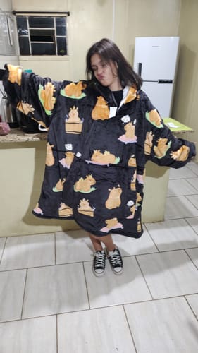 Cliente vestindo o grande Sleepo Capivara preto e mostrando seu tamanho com os braços abertos.
