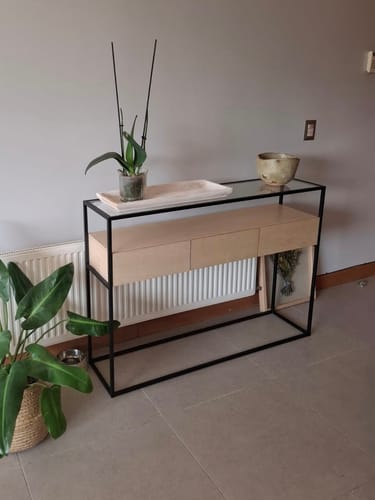 Cliente mostrando su arrimo SILA 3 cajones de madera clara y estructura negra en un living.