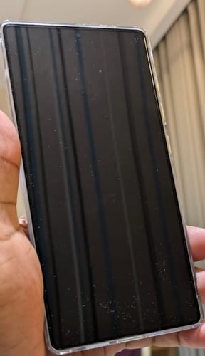 Customer's hand holds a smartphone with the UltraShield Tempered Glass applied, showing its fit on the dark screen.