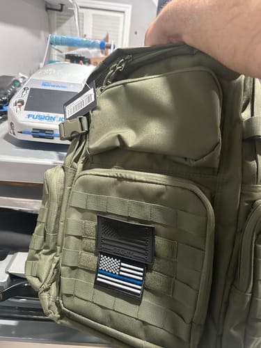 Customer holding a green Commando Backpack with a custom patch on the front webbing.