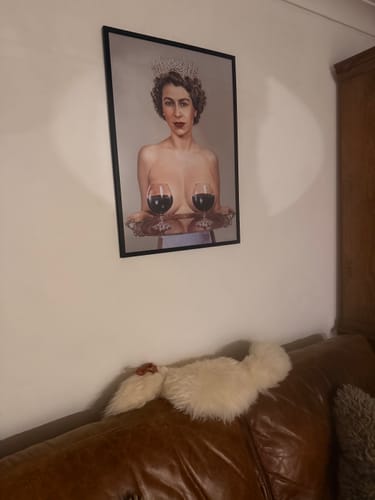 Customer's framed art print of a queen with wine glasses, displayed on a wall above a leather sofa.