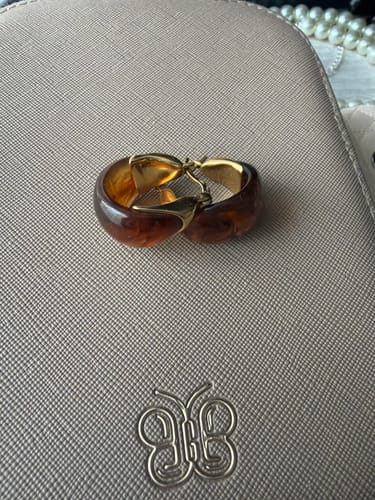 Customer's Brown Tahiti Hoop Earrings on a surface, showing the brown wood-like pattern and gold accents.