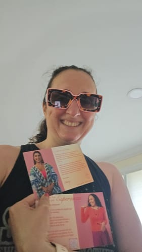Customer smiling while wearing the stylish Deco Sunglasses and holding up brand postcards.