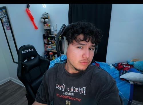 Reviewer wearing a dark, graphic AOT x YLA Classic Tee while sitting indoors with headphones on.
