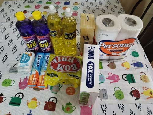 Cliente exibe os produtos de limpeza do Cesta Kit Limpeza Plus, incluindo desinfetante e detergente, em uma mesa.