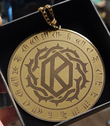Customer's large, gold custom logo pendant, engraved with a detailed design, shown inside its black presentation box.