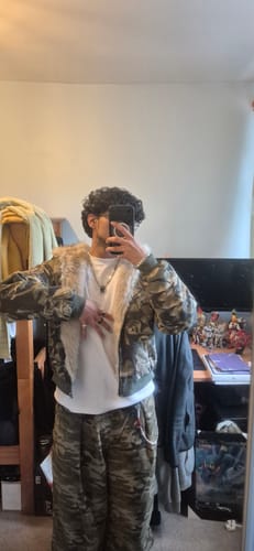Reviewer wearing the camouflage bomber jacket open, showing the fluffy faux fur lining against a white shirt.