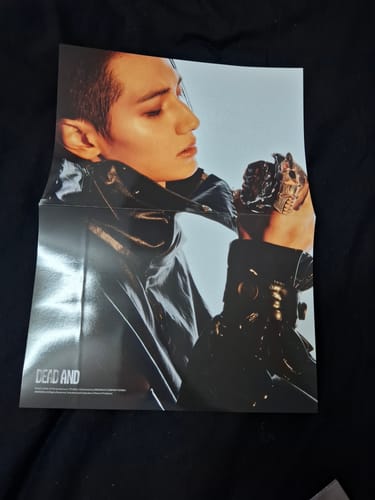 Customer's folded poster from the XDINARY HEROES - DEAD AND album, showing a member in a shiny black outfit holding a skull.