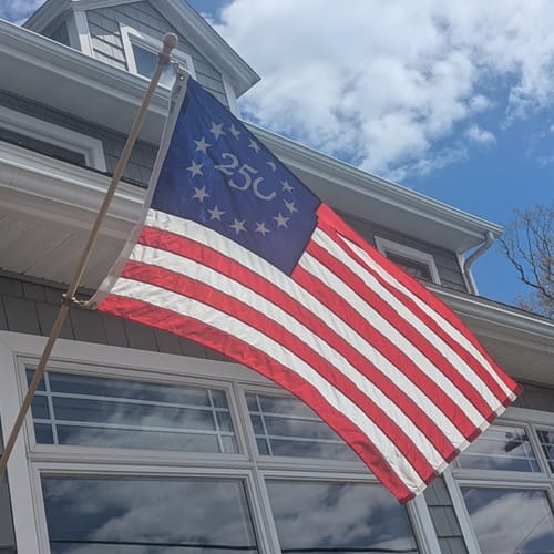 Customer's America 250™ flag from the stick flag set flying on a flagpole outside their house.