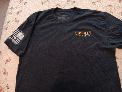 Customer's heather gray "250 Years of Heroes" tee laid out, showing the front with "Liberty Since 1776" text and a sleeve patch.