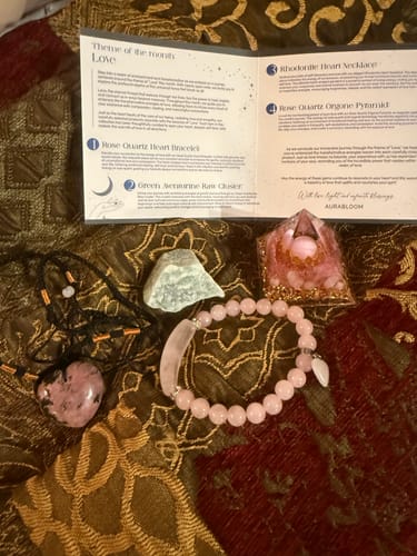 Reviewer's monthly VIP Crystal Club set with a pink stone bracelet, necklace, pyramid, and green crystal on a cloth.