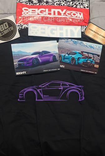 A customer's black 80Eighty® DCG88 Shirt with a purple sports car outline, displayed flat with stickers and postcards.