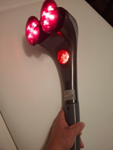 Vásárló kezében tartja a bekapcsolt, vörösen világító infravörös izomlazító masszírozót.
