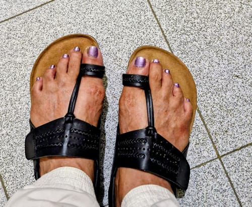 Customer's feet wearing the black Frido Puneri Chappals with a brown footbed, seen from above.