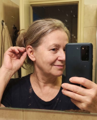 Vásárló mutatja a fülébe helyezett diszkrét Whisper+ Pro hallókészüléket egy tükörben.