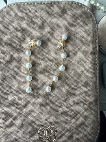 A customer's pair of Pearl Drop Earrings with a delicate gold chain and multiple pearls laid on a textured case.