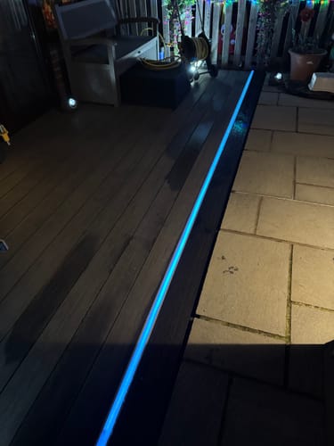 Customer's recessed profile installed between a deck and patio, glowing with a bright blue light at night.