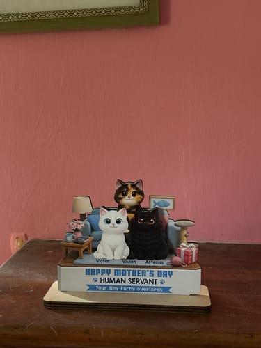 Customer's personalized wooden plaque showing three illustrated cats—white, black, and calico—on a couch, displayed on a wooden table.