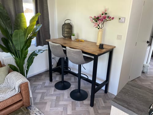 Recensent toont de industriële bartafel met houten blad en zwart onderstel in een woonkamer, met twee grijze barkrukken.