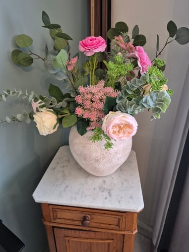 Recensent toont het Boeket Flora in een lichte, getextureerde vaas op een houten bijzettafeltje.