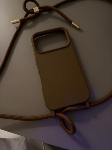A Cordinha Odara Mocha Mousse DOURADA de um cliente, conectada a uma capa de celular de cor correspondente.