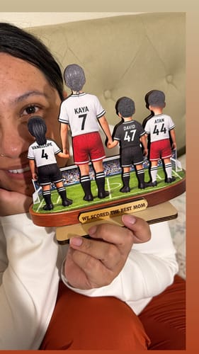 Customer holding the personalized wooden plaque of a soccer mom and three kids with custom names on their jerseys.