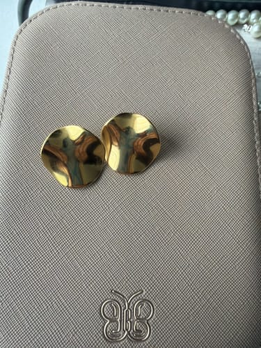 Customer's pair of wavy, gold Tyra Earrings resting on a textured case, showing their shiny surface.