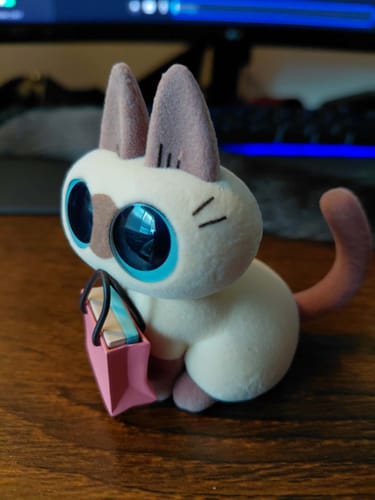 Customer's cute Nobeko Azukisan cat figure with large blue eyes holding a pink shopping bag.