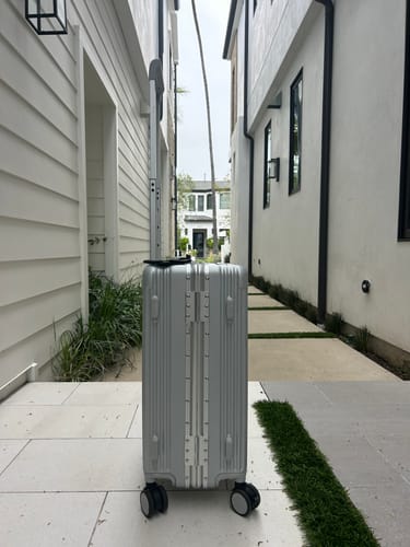 Reviewer's silver hard-shell luggage with an extended handle, standing on an outdoor patio.