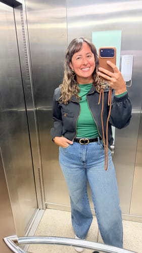 Cliente tirando uma selfie no espelho de um elevador, usando a Cordinha Nora na cor mocha para segurar o celular.