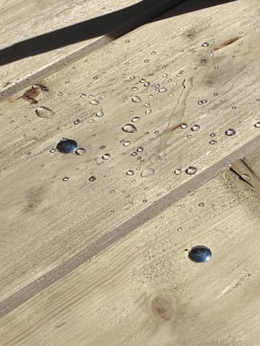 Klant toont het waterafstotende effect van ProFluid Care 102 op houten planken, met parelende waterdruppels.