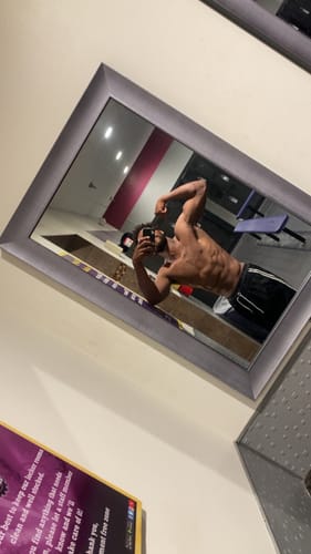 Customer's mirror selfie flexing a bicep, showing defined abs after using the muscle gain playbook.