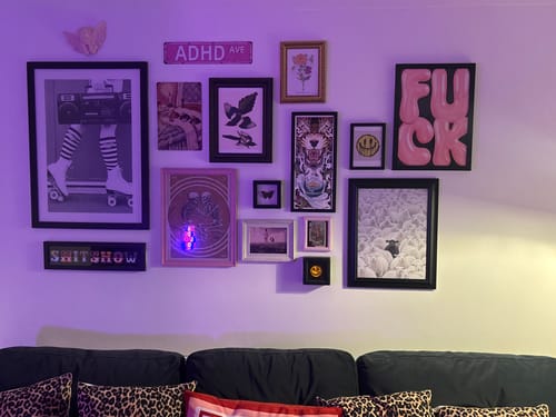 Customer's 'The Black Sheep' print in a black frame, displayed on a purple-lit gallery wall over a sofa.