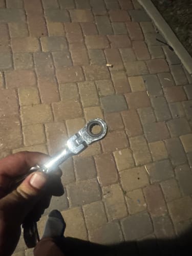 Customer holding the shiny 10mm Wrench Keychain in their hand over a paved surface.