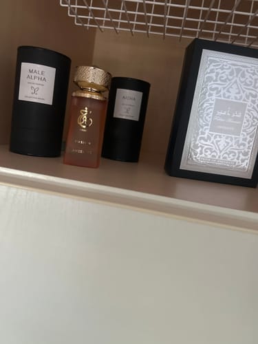 Photo d'un client montrant le parfum Khair Fusion avec son bouchon doré sur une étagère, à côté de son emballage noir.