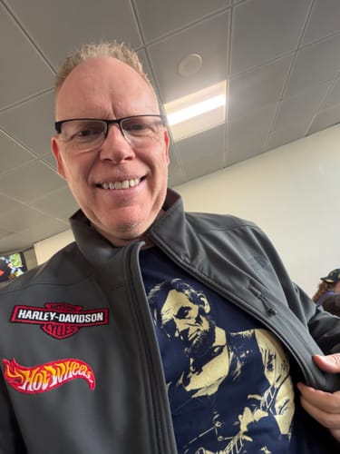 Reviewer smiling and pulling open a jacket to show the blue Lincoln Guitar T-Shirt underneath.