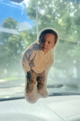 Reviewer's custom air freshener with a photo of a child, cut to shape and hanging in a car.