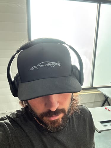 A reviewer in a close-up shot wearing the black 80Eighty® Limited Edition DCG89 Hat with headphones on top.