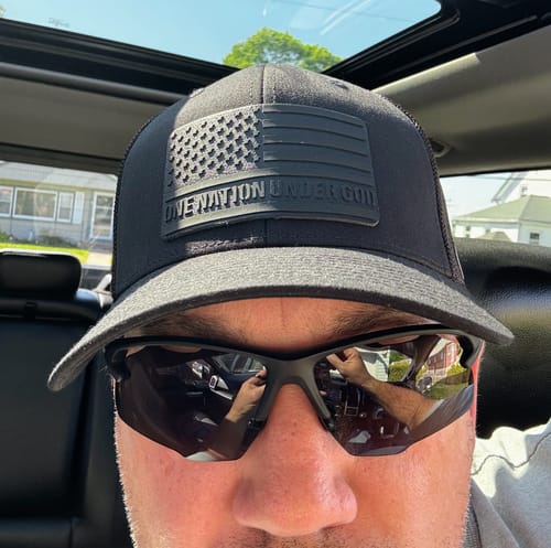 A close-up of a customer wearing the black One Nation Under God Blackout Version patch hat in a car.