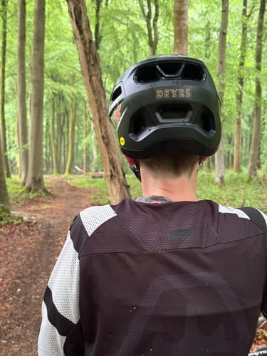 Customer from behind wearing the black and white Revenant Long Sleeve Jersey and a helmet on a forest trail.