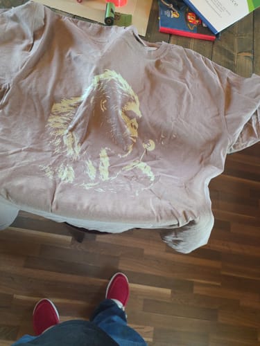 A customer's brown Blowing Wishes T-Shirt laid out on a surface, showing the front graphic.