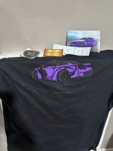 Customer's new black DCG88 Shirt with a purple car graphic laid out with included stickers and photo.