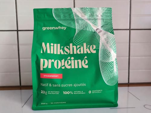 Un client montre le sachet vert du Milkshake protéiné saveur fraise sur un comptoir de cuisine.