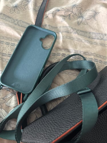 Cliente mostrando a Case Oliva verde junto a uma bolsa com alça da mesma cor em uma superfície estampada.